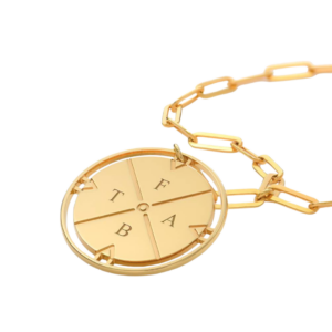 A close-up of a delicate gold compass necklace with intricate detailing, hanging from a gold chain. The compass pendant symbolizes adventure and exploration, making it a meaningful and stylish gift for women who travel.